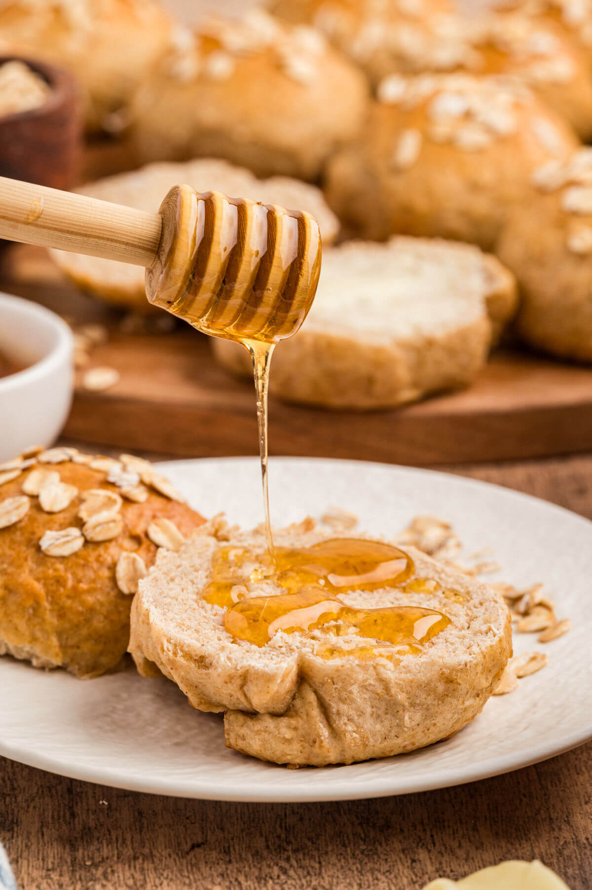 An oatmeal roll being drizzled with honey.