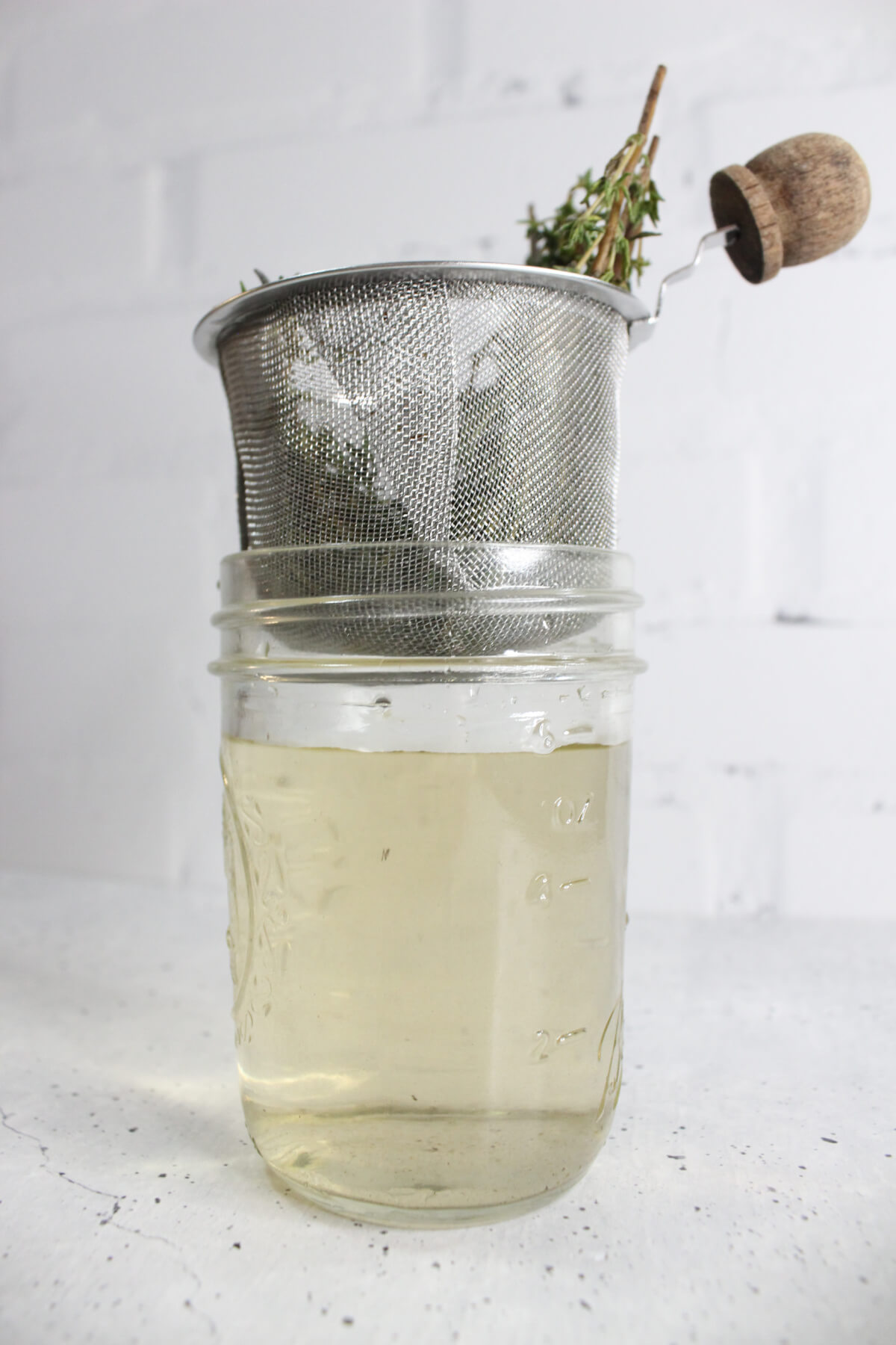 mason jar with thyme-infused water and a fine mesh sieve sitting on top of the jar with thyme sprigs in it
