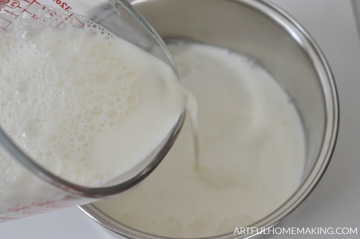 Cup pouring milk into a saucepan.