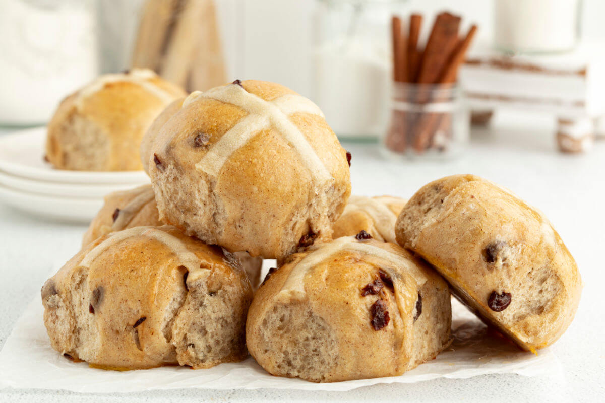 Photo of 6 baked sourdough hot cross buns in a pile on a white tabletop.