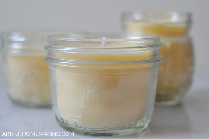 three beeswax candles in mason jars on a marble countertop