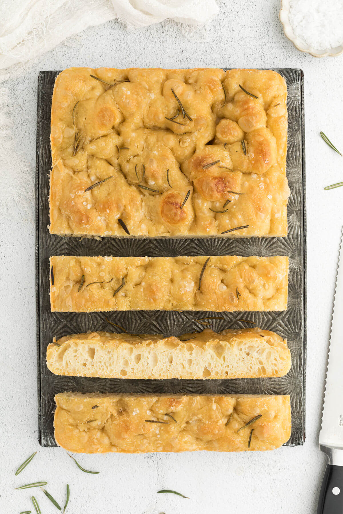 top down view of sourdough focaccia bread on a metal sheet with three slices sliced from loaf