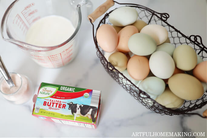 glass measuring cup with milk, wire basket of eggs, box of butter