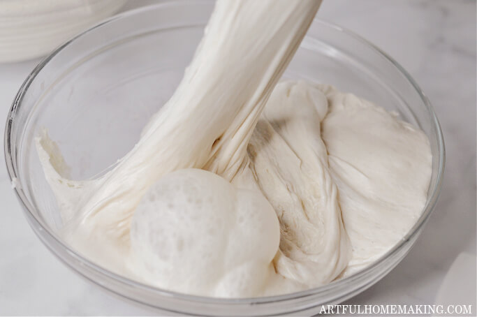 stretching and folding sourdough in a glass bowl with large bubbles in dough