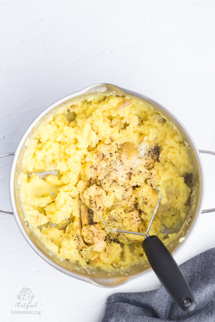 mashing potatoes in a stock pot with a potato masher