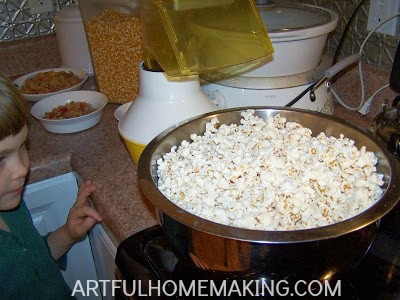 a child standing next to a large metal bowl filled with freshly popped popcorn