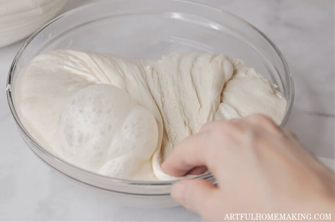 hand folding sourdough bread in glass mixing bowl