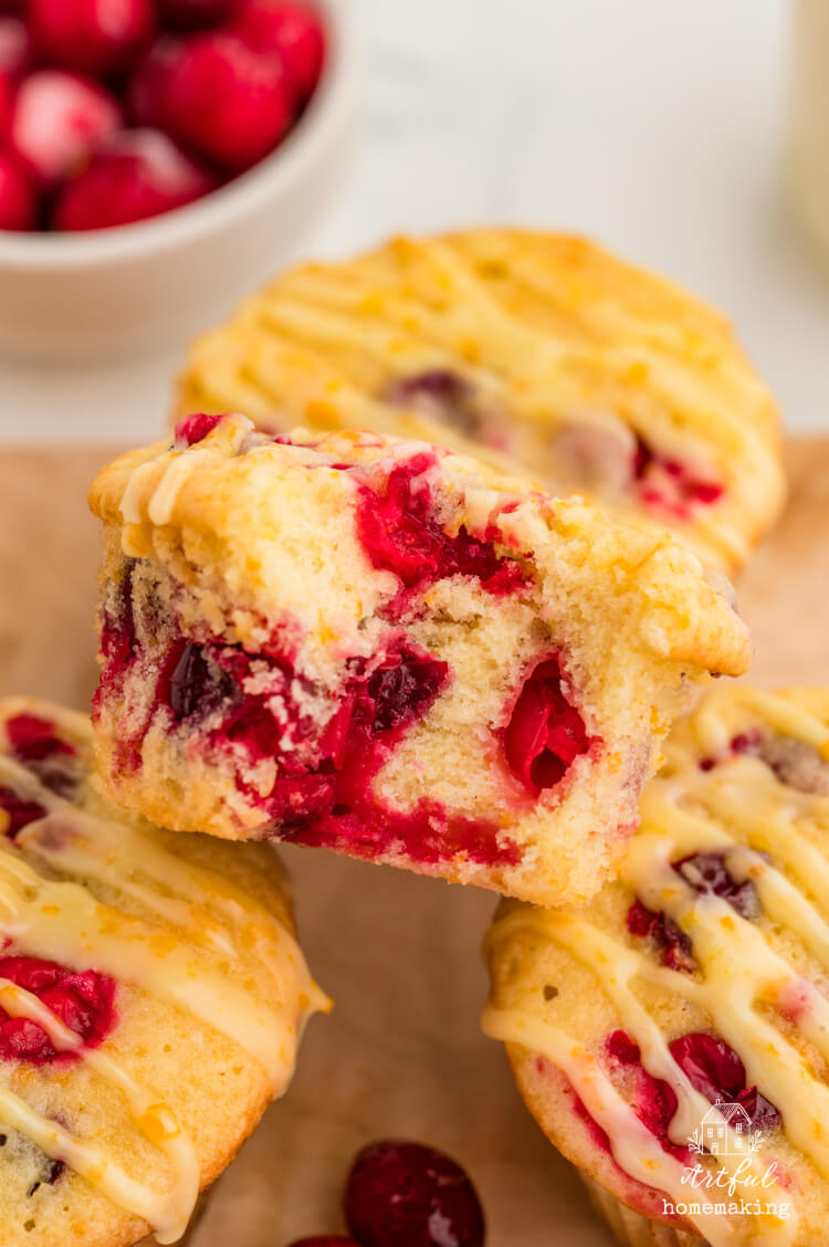 a pile of cranberry orange muffins on parchment paper with a bowl of cranberries in the background