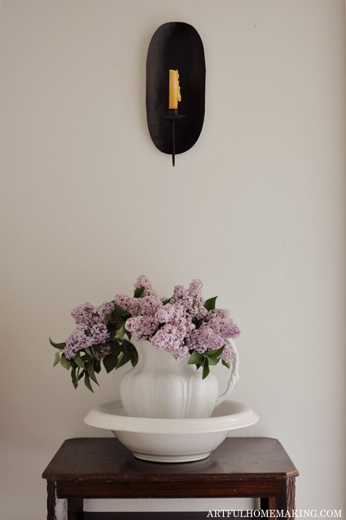 white ironstone pitcher filled with purple lilacs on a wooden stand 