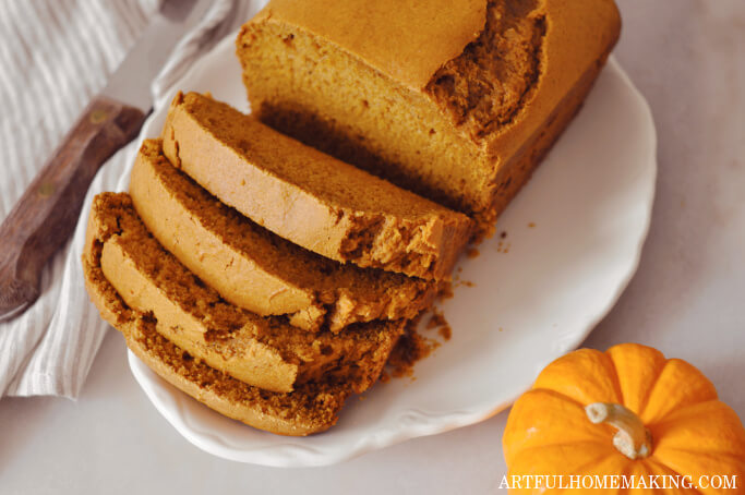 Sliced sourdough pumpkin bread on a white platter with a mini pumpkin next to it.