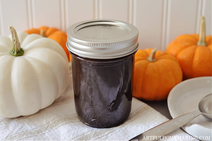 mason jar of homemade pumpkin spice coffee syrup surrounded by small white and orange pumpkins