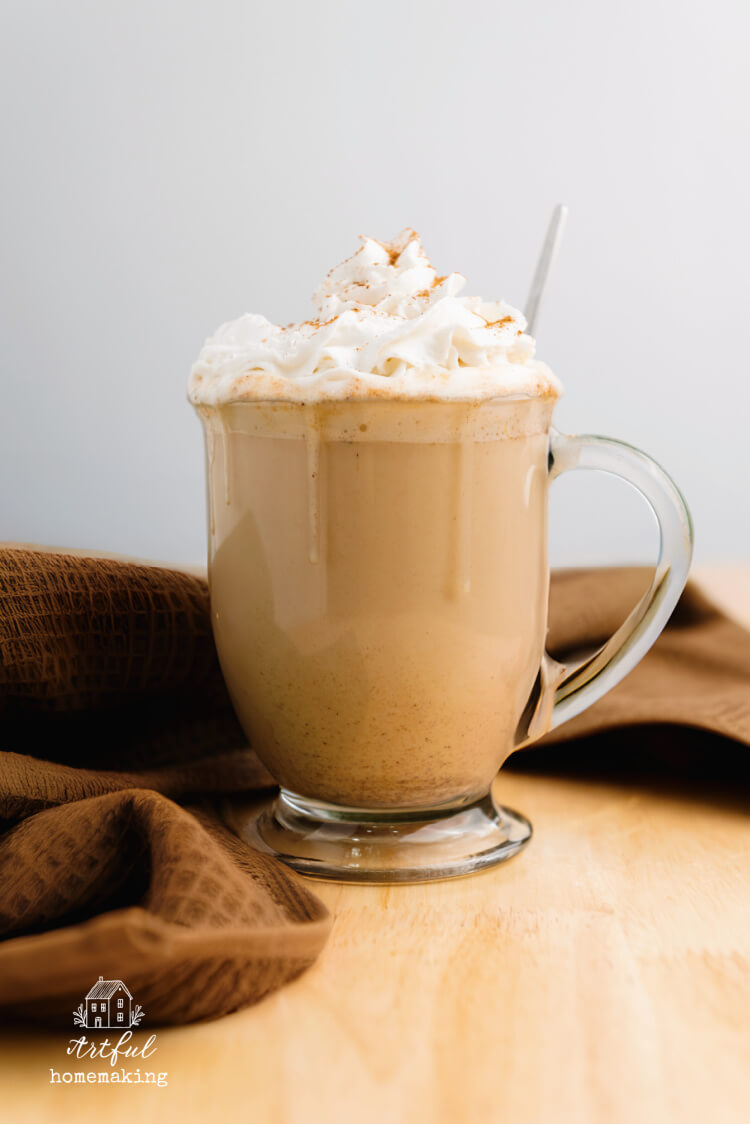 glass mug of pumpkin spice latte with a brown towel next to it on a table