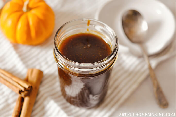 homemade pumpkin spice syrup in a jar with an orange pumpkin and two cinnamon sticks next to it