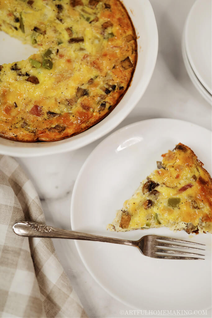 a piece of crustless quiche on a white plate sitting next to a pie dish of quiche with one slice missing