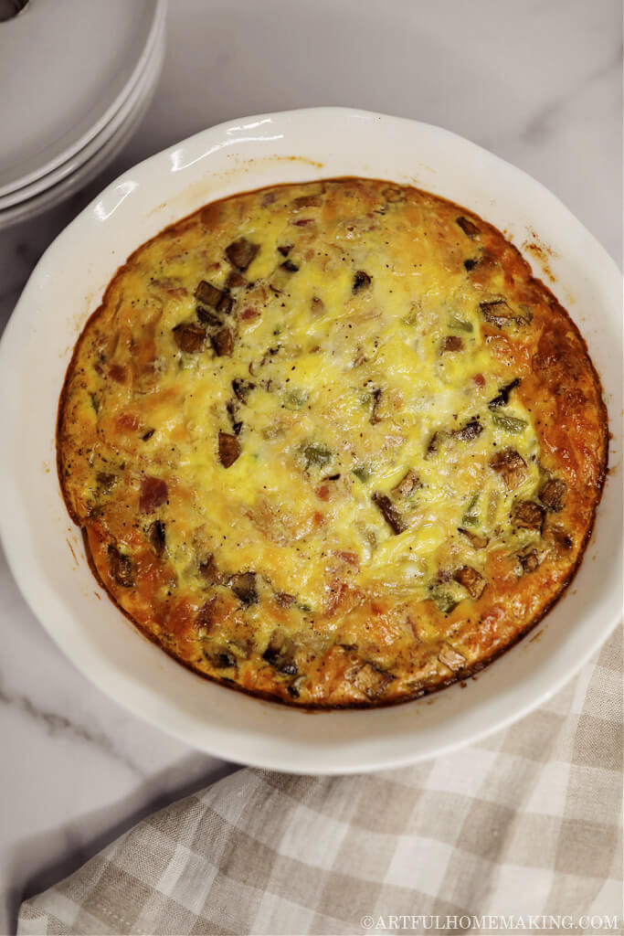 crustless quiche in a white ceramic pie dish with a beige and white checked linen dish towel