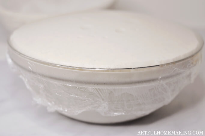 glass bowl with plastic wrap on top showing sourdough that has doubled in size after bulk fermentation