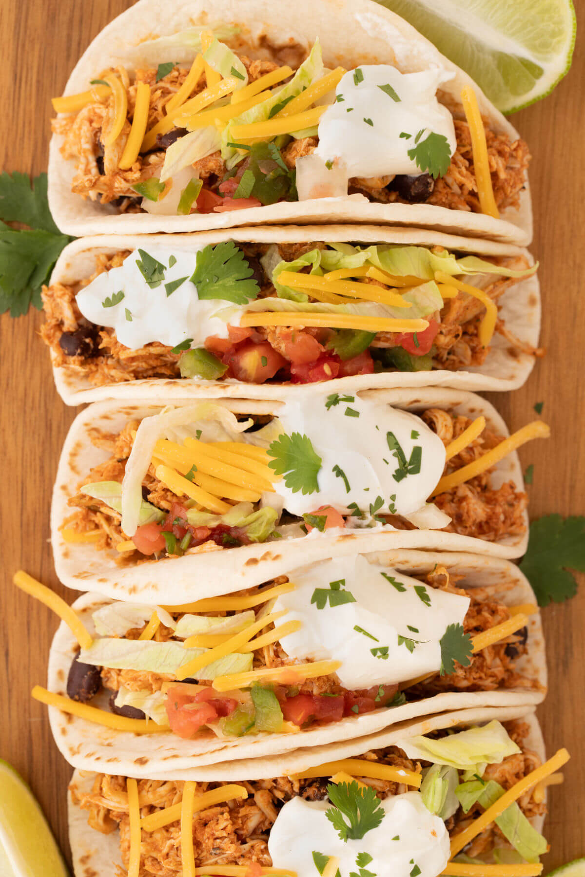 Rotisserie chicken tacos with filling ingredients like cheese, sour cream, and tomatoes on a wooden cutting board..