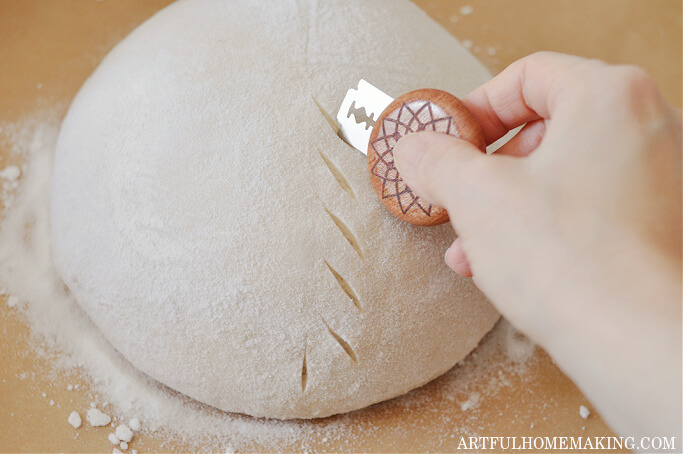 sourdough bread boule on parchment with hand scoring leaf design on bread