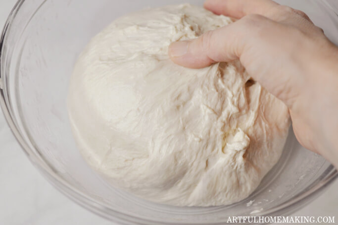 photo shows hand picking up dough from glass mixing bowl to transfer to banneton basket