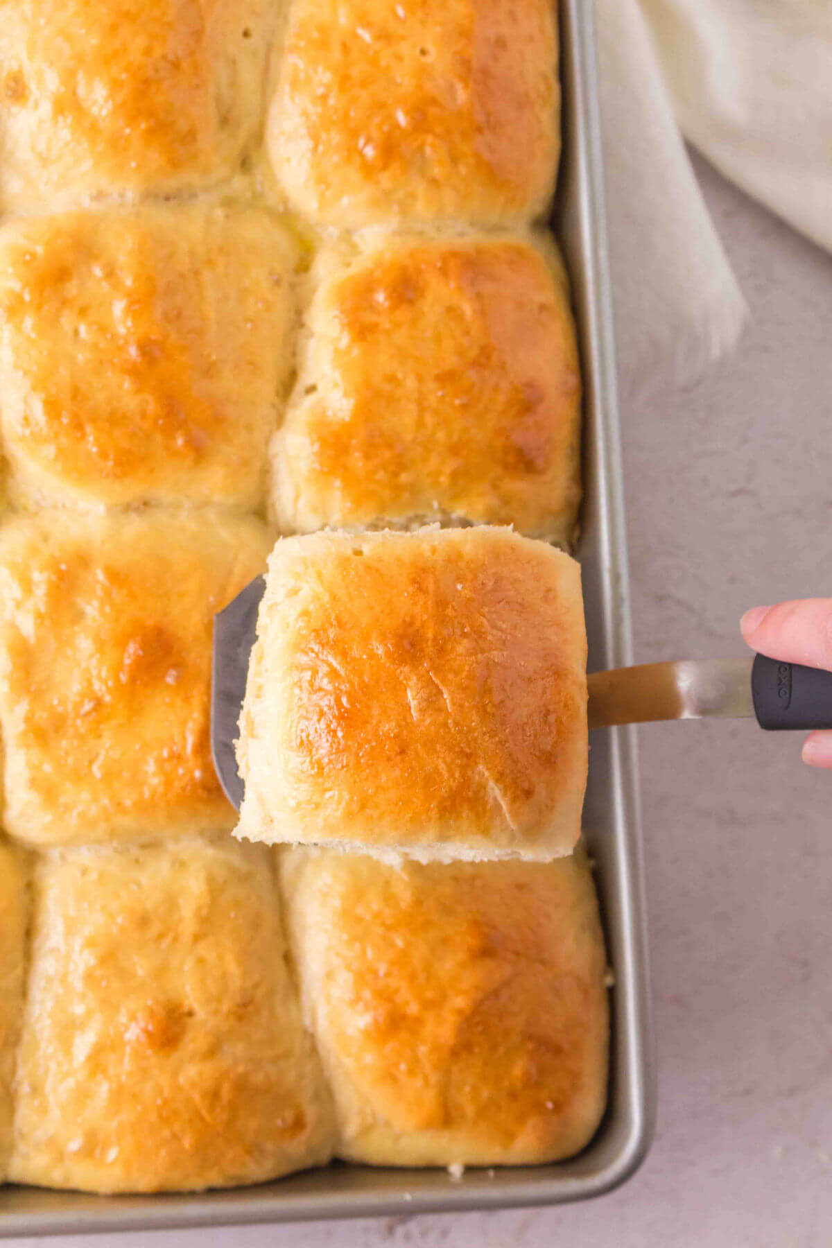 Pan of sourdough discard rolls after baking, with one roll being lifted up on a spatula for serving.