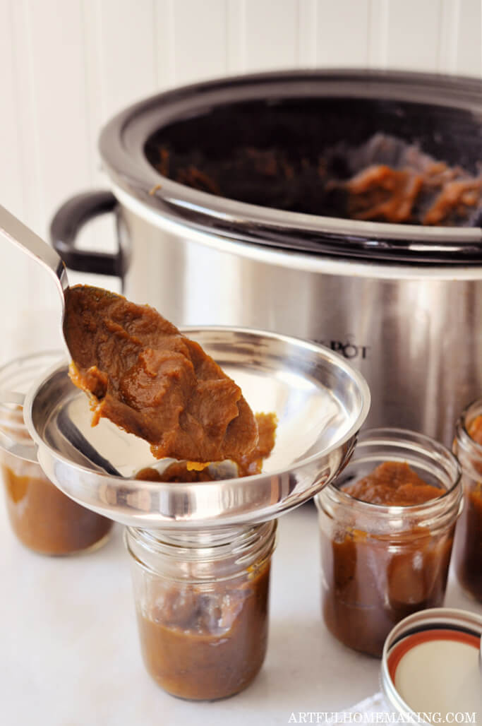 spooning completed pumpkin butter in a jar with a spoon and funnel in the jar