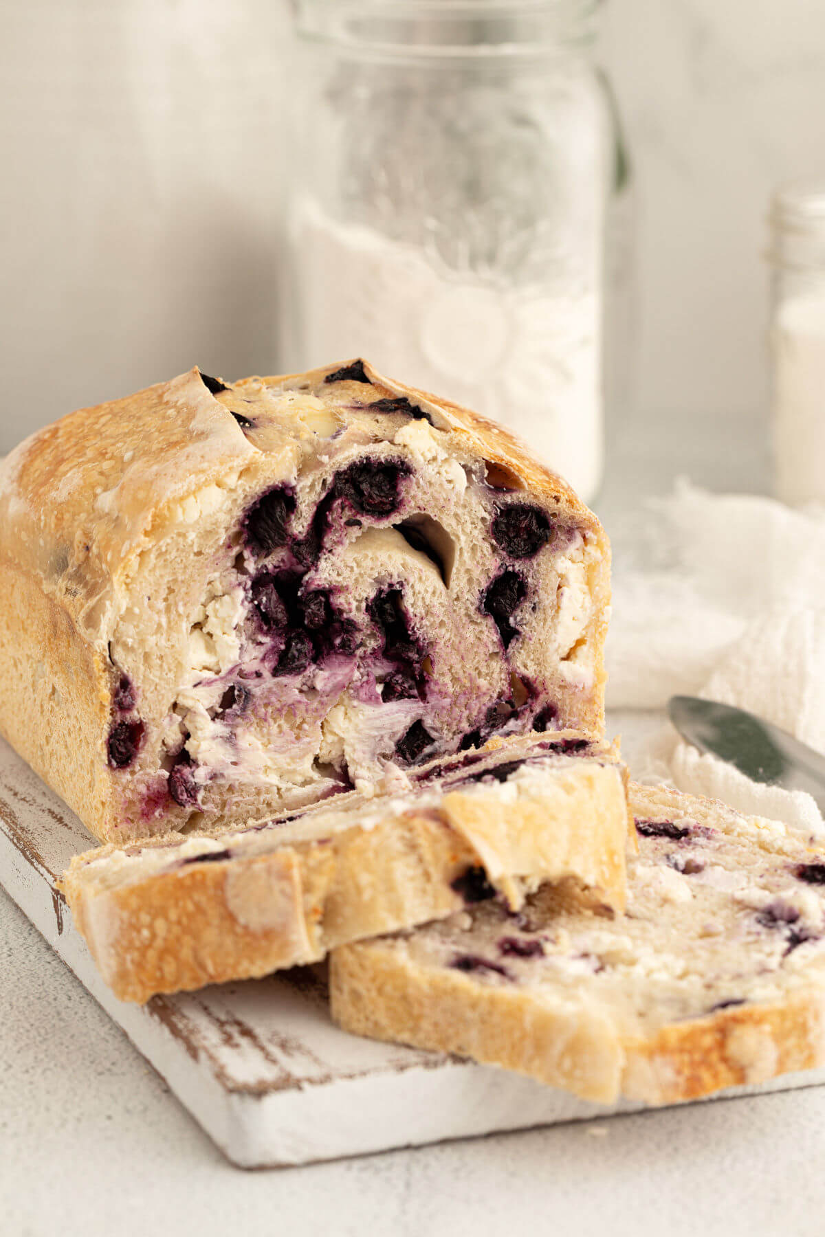 blueberry cream cheese sourdough bread loaf on a white board with a jar of flour in the background