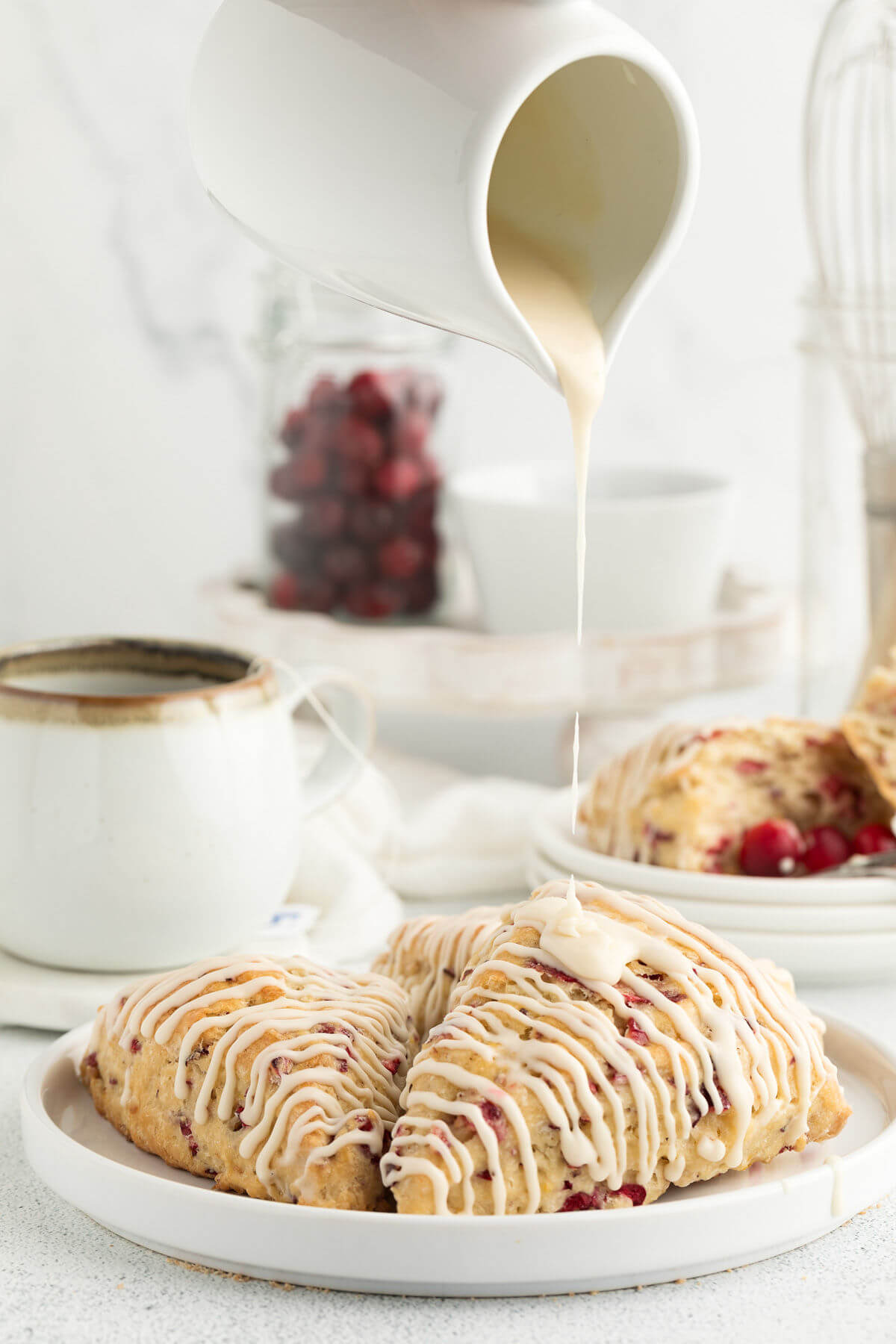 sourdough cranberry orange scones on a white plate with a small white pitcher drizzling glaze on the scones
