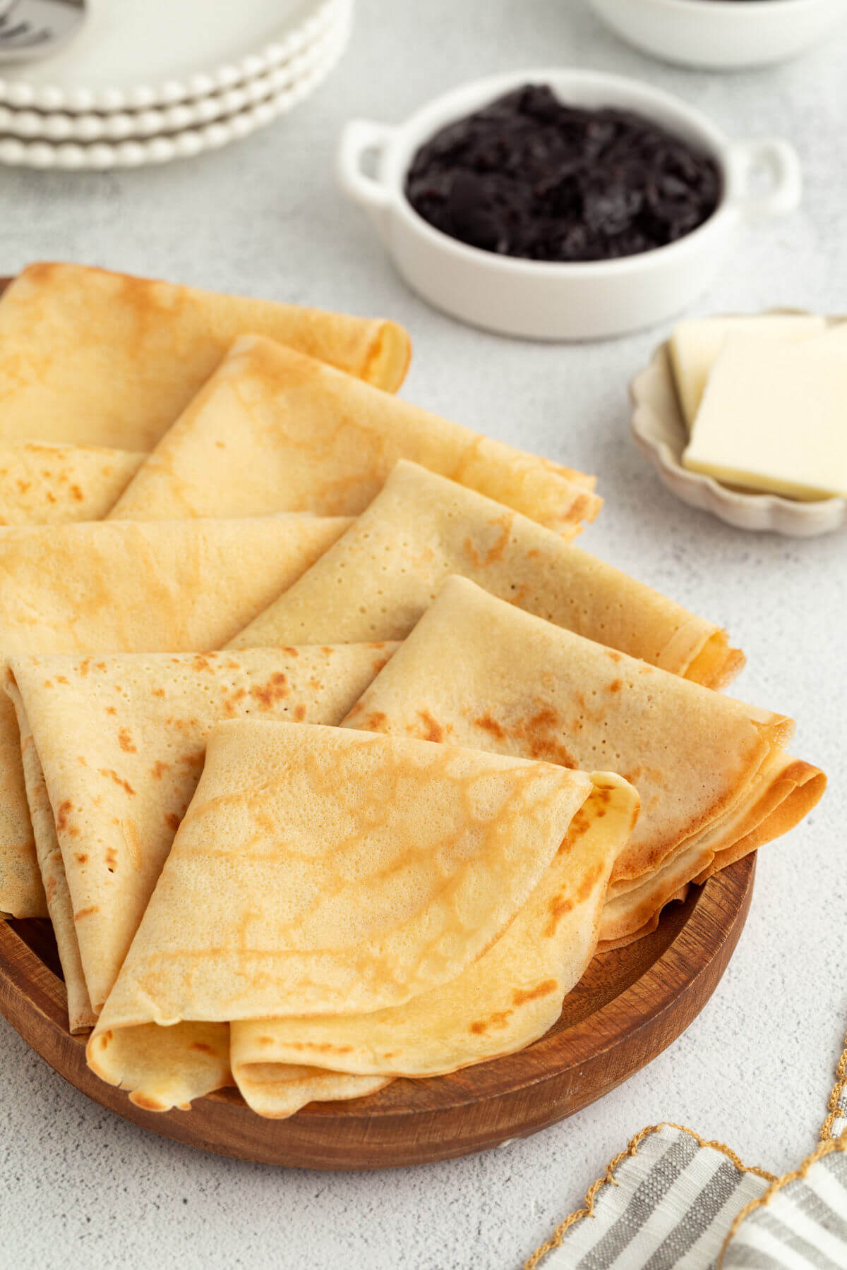 Homemade sourdough crepes folded up on a wooden serving tray.