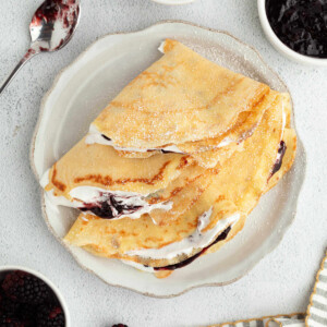 Sourdough crepes on a plate with whipped cream and fruit.
