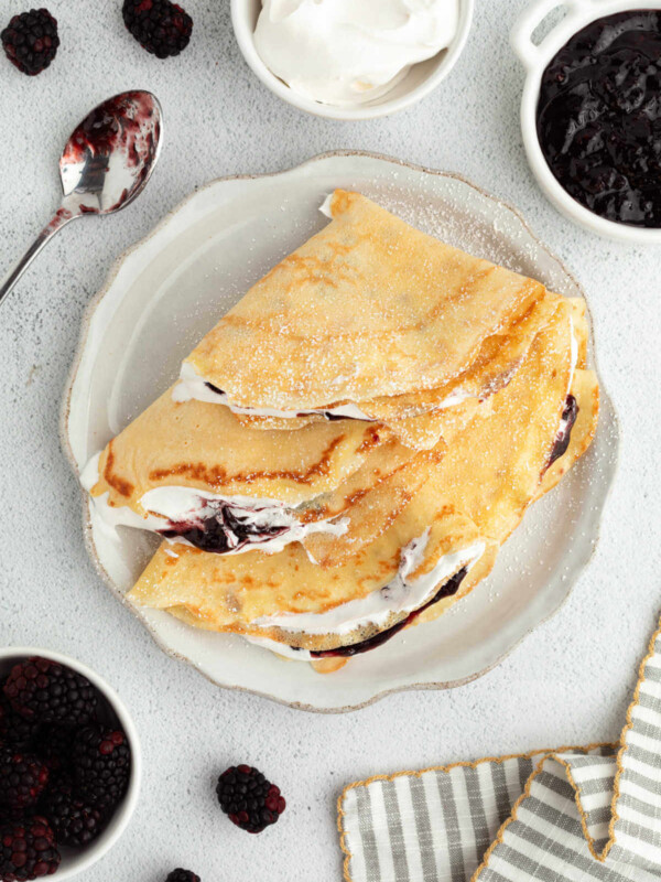 Sourdough crepes on a plate with whipped cream and fruit.