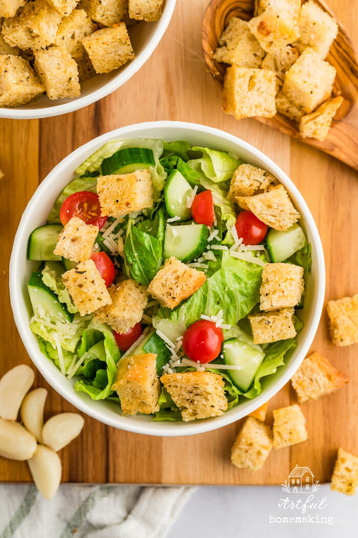 white bowl with green lettuce salad, cucumbers, cherry tomatoes, parmesan cheese, and sourdough croutons