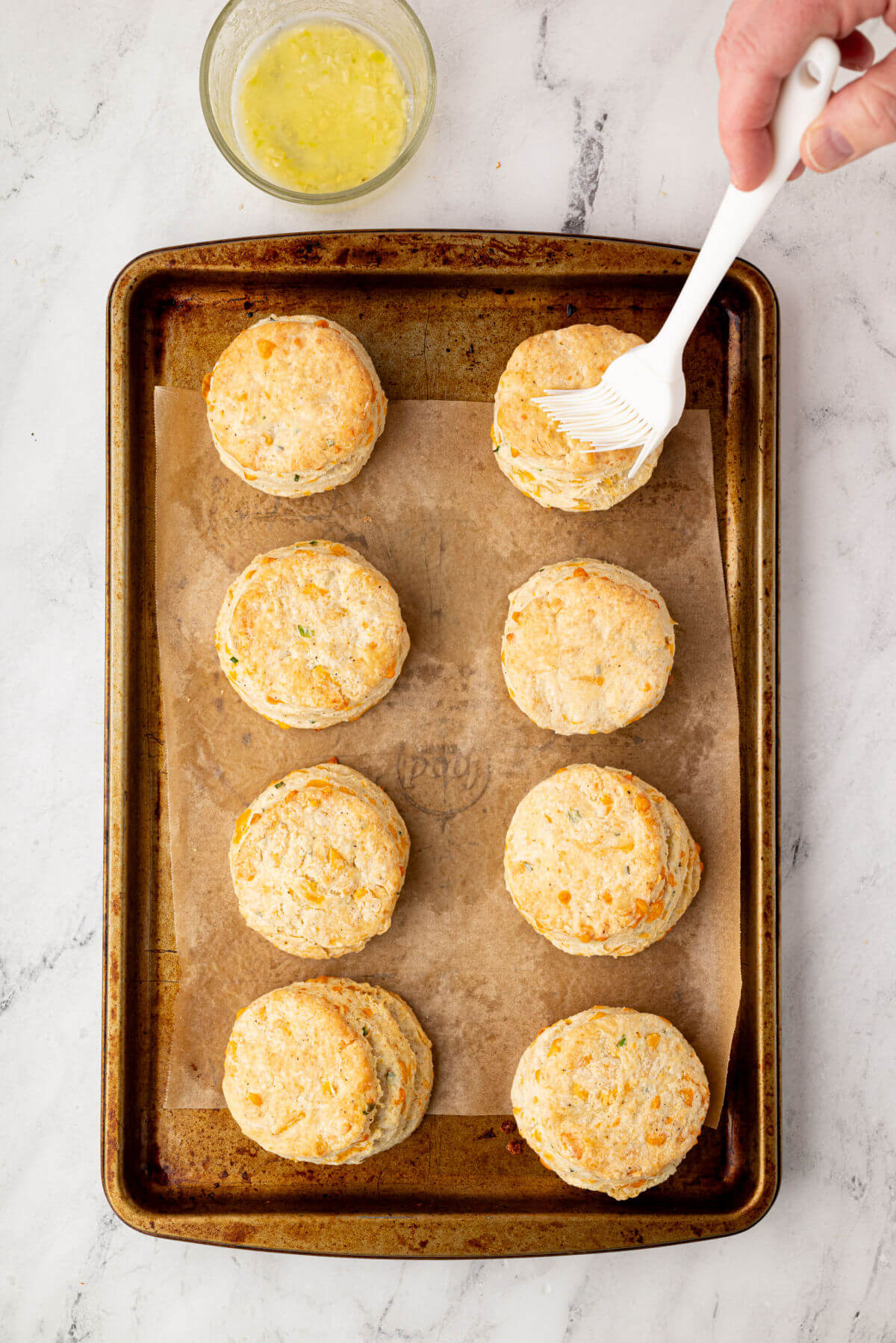 Baked sourdough cheddar biscuits being brushed with garlic butter.