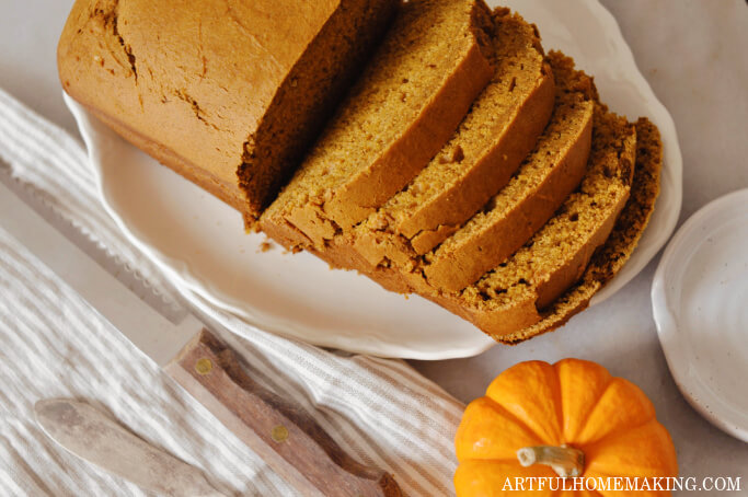 sourdough pumpkin bread on a a platter with a bread knife and a mini pumpkin next to it