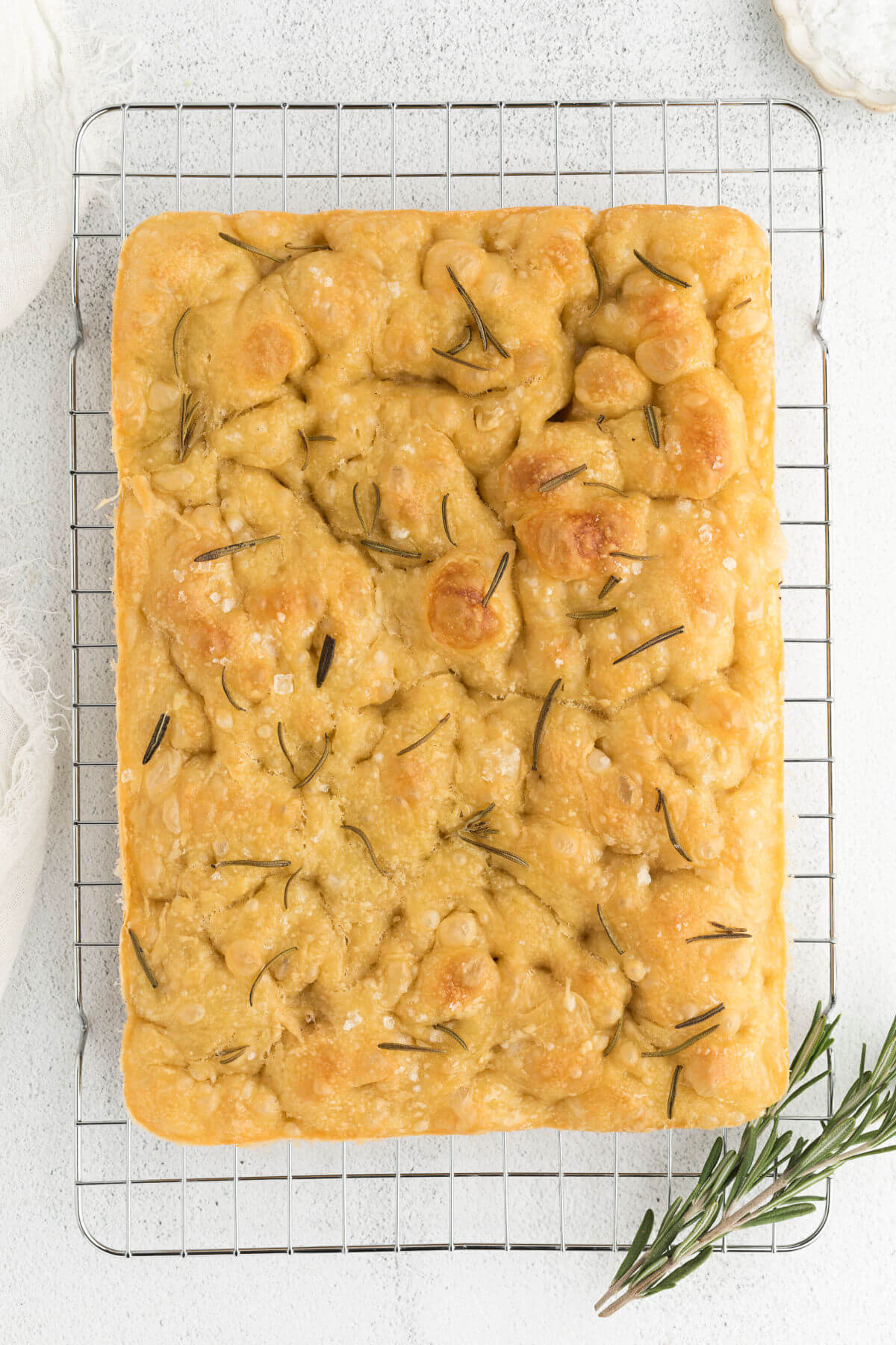 baked sourdough focaccia bread on a wire cooling rack with fresh rosemary sprigs