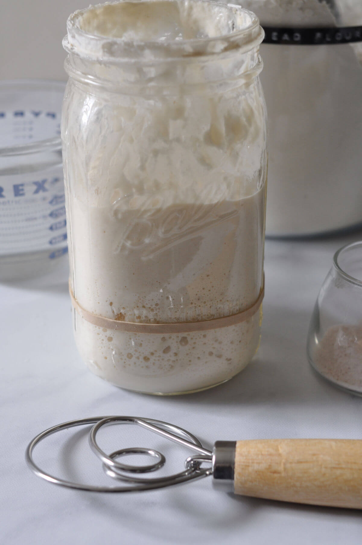Danish dough whisk next to a jar of risen sourdough starter.
