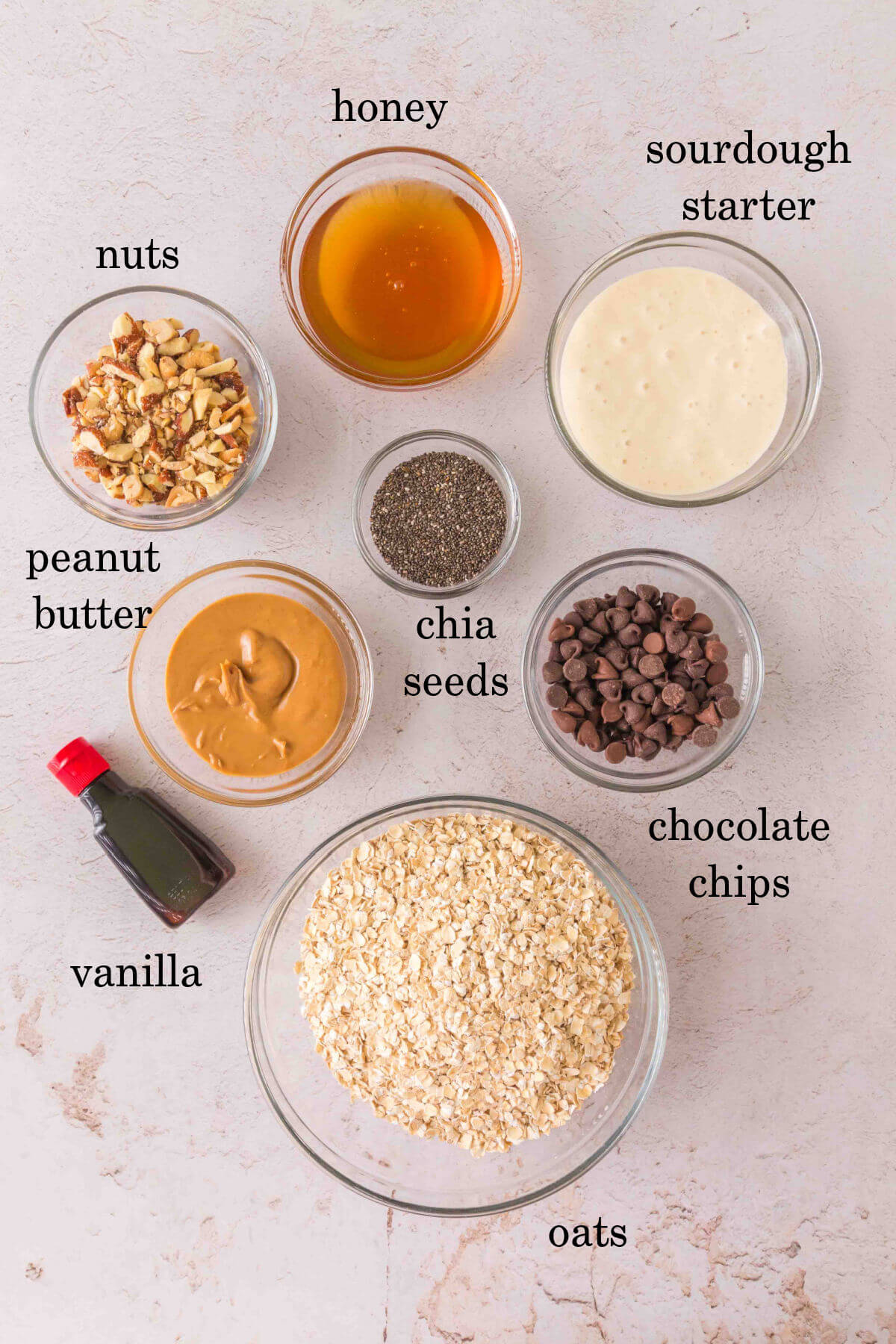 Sourdough granola bar ingredients in small bowls with text overlay labeling each ingredient.