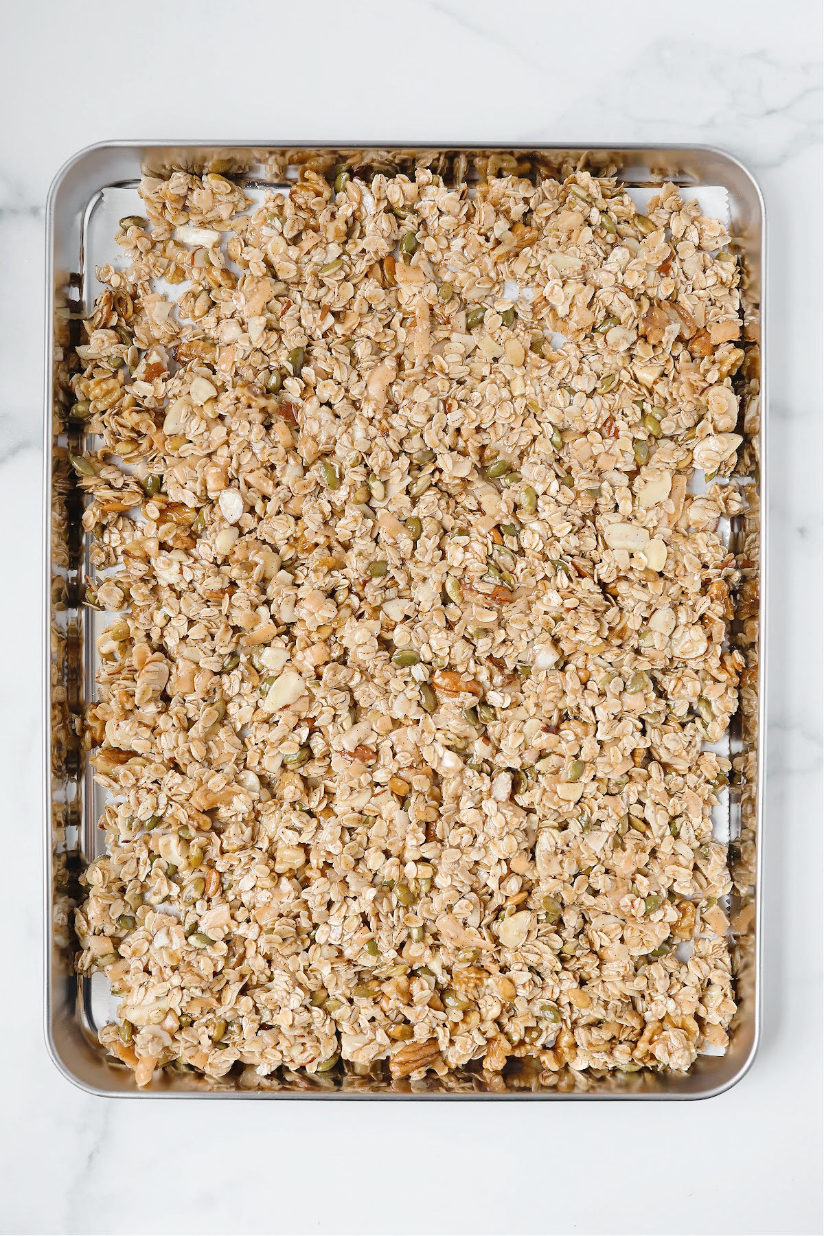 Sourdough granola pressed onto a parchment-lined sheet pan, ready to bake.