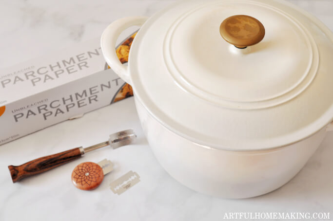 Dutch oven, parchment paper, and two bread lames on counter