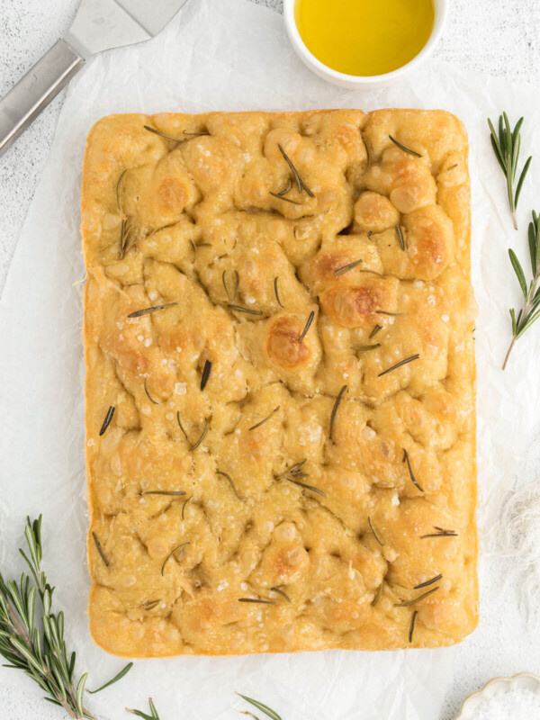 top down view of sourdough focaccia on a white counter with a bowl of olive oil and rosemary sprigs