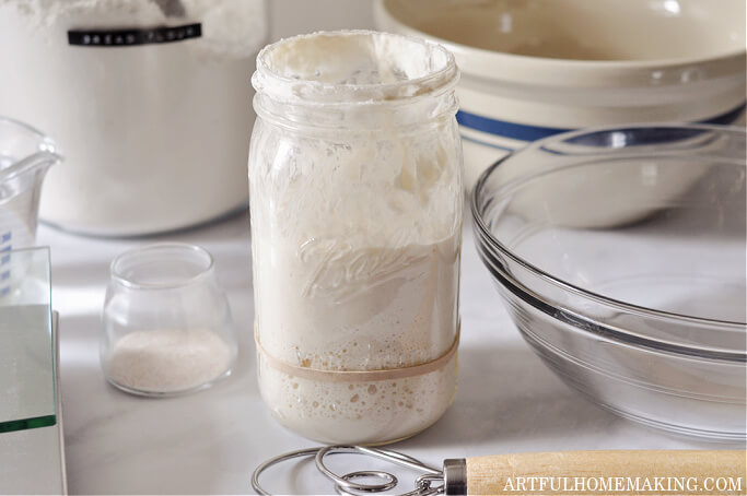 sourdough starter with mixing bowls, flour jar, and dough whisk