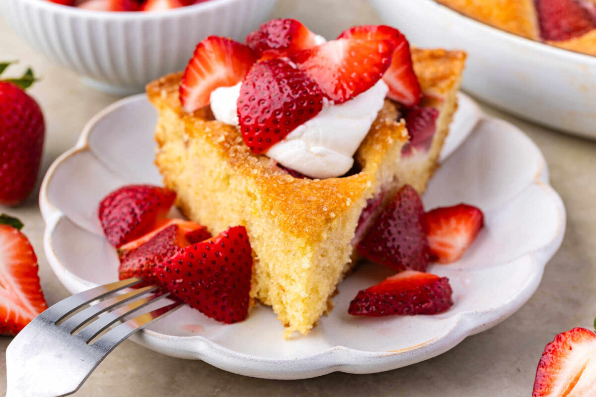 Slice of sourdough strawberry cake on a plate with whipped cream and fresh strawberries.