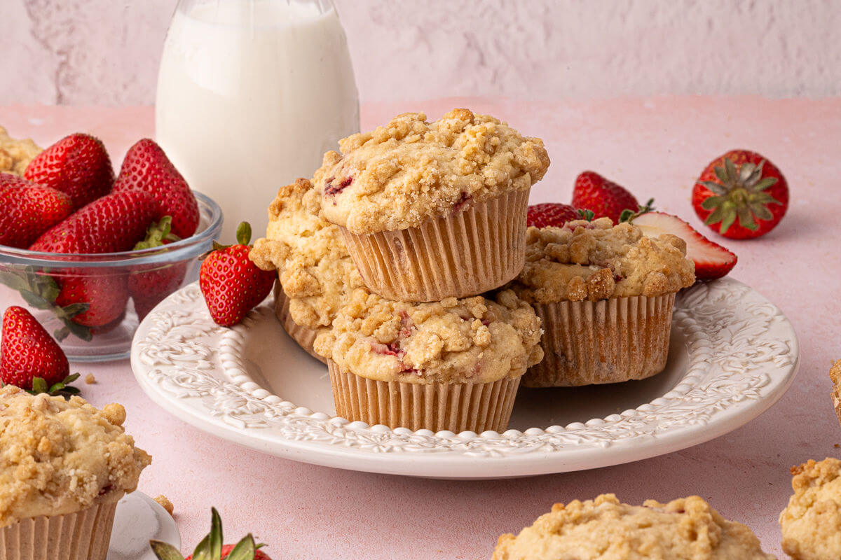 Sourdough strawberry muffins on a plate with a bowl of strawberries and a glass of milk behind them.