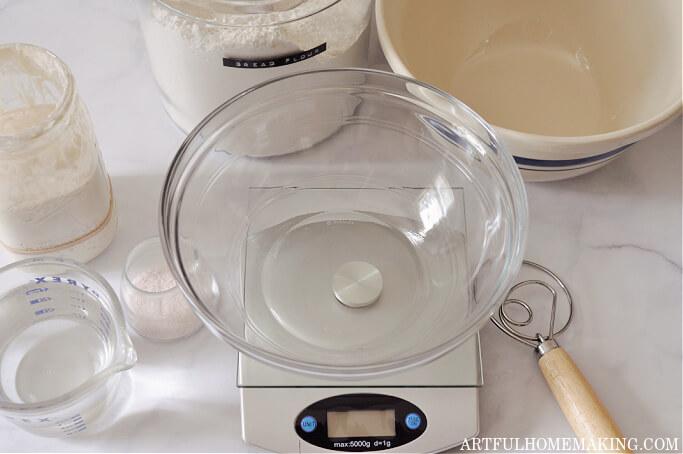 sourdough bread baking supplies, including mixing bowl, jar of flour, digital scale, dough whisk