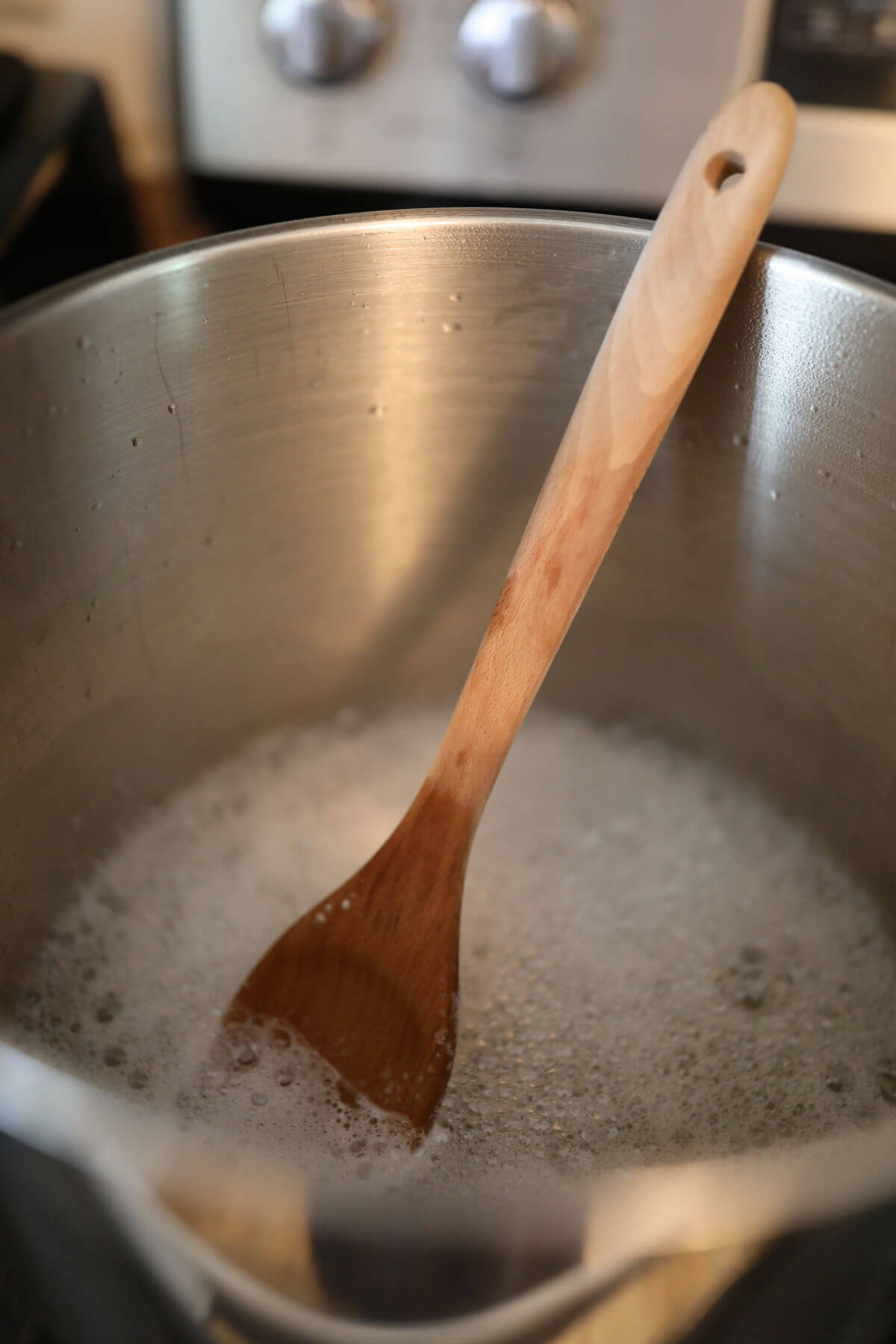 Large stock pot with water, soap and a wooden spoon in it.