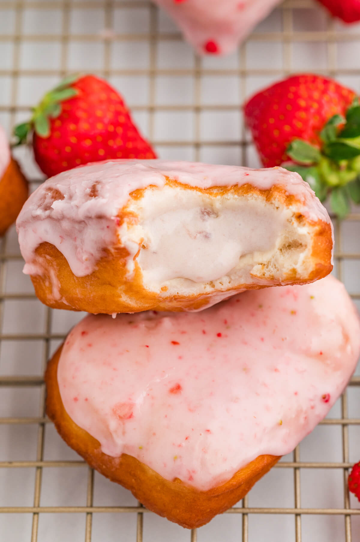strawberry donuts on a wire cooling rack and one has a bite taken out of it, showing the custard filling oozing out