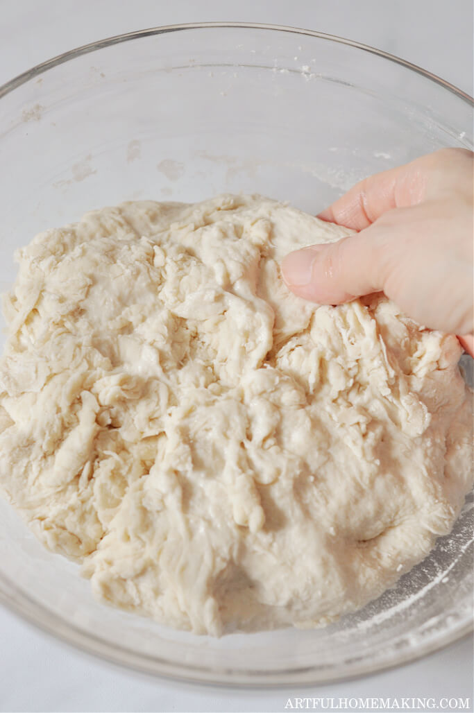 photo of sourdough in glass bowl and hand starting to stretch dough