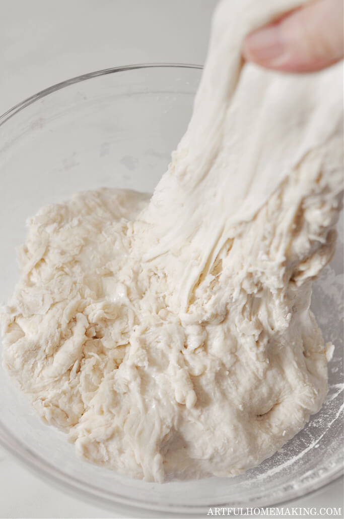 photo shows hand stretching sourdough upwards during stretch and fold