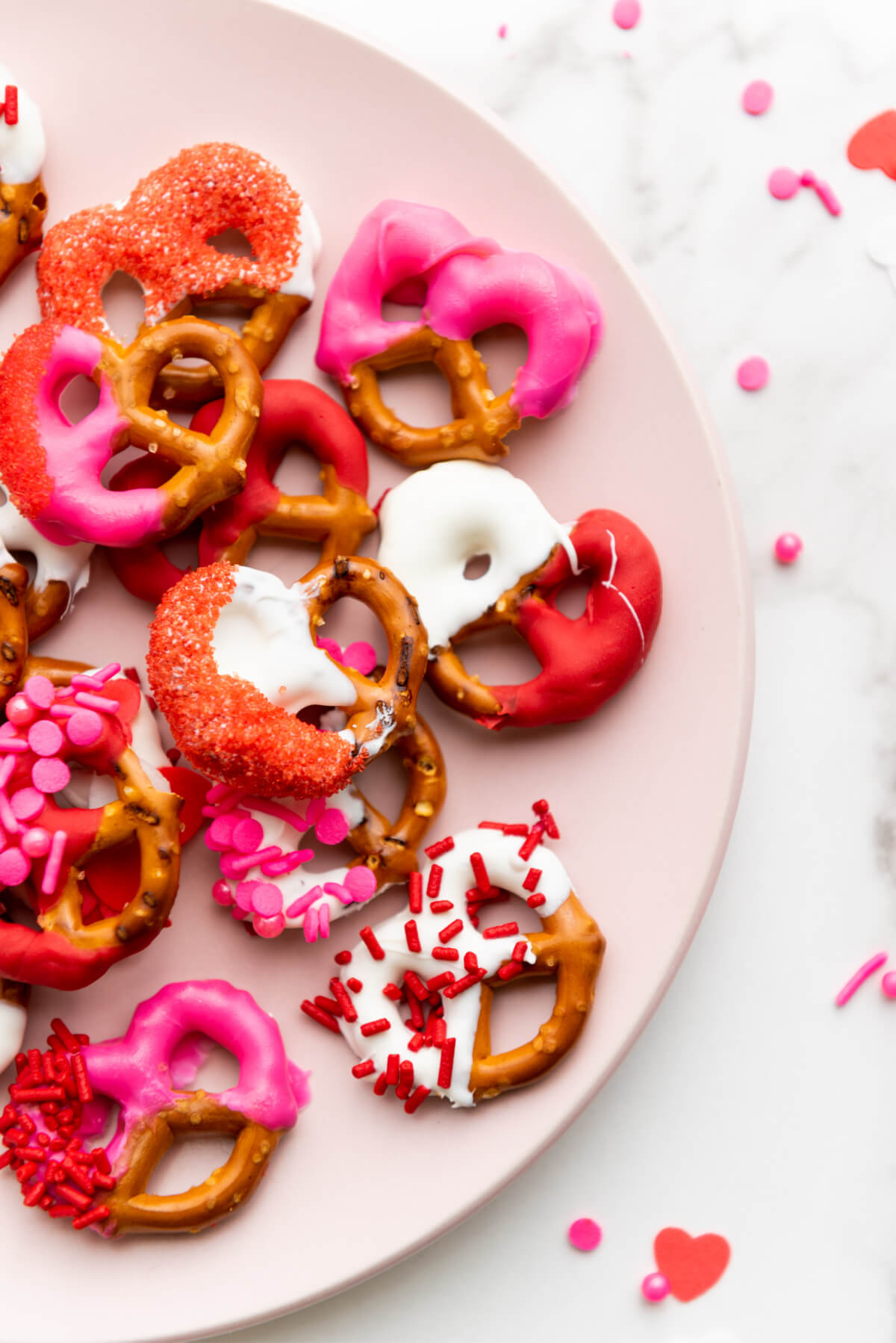 top down view of Valentine's day pretzels coated with pink, white and red melted candy on a pink plate