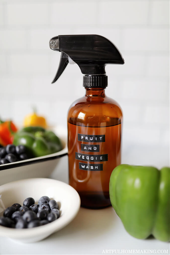 amber spray bottle with fruit and veggie wash label next to a bowl of blueberries and a green bell pepper