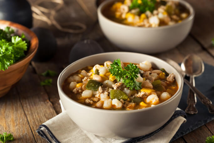 two white bowls of chili with white beans and chicken on a wooden table